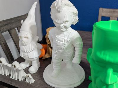 Collection of unpainted 3D printed Halloween figures including a gnome, doll, and Frankenstein head